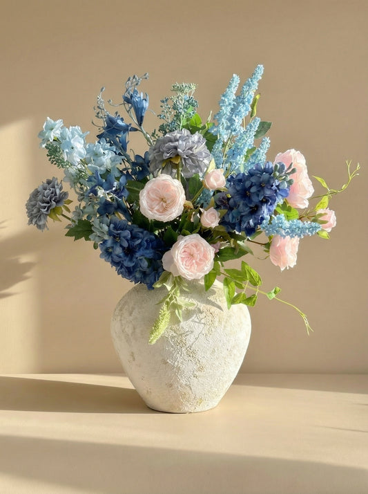 Bouquet of blue and pink flowers in a textured white vase on a beige background