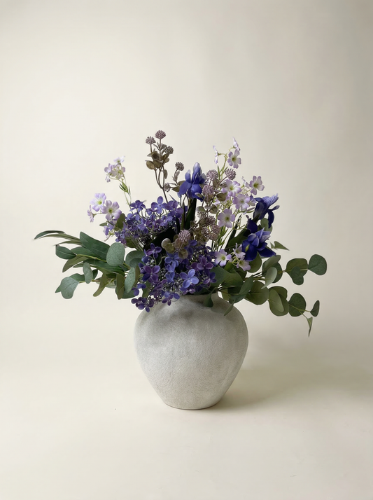 Bouquet of purple flowers in a gray vase on a light background