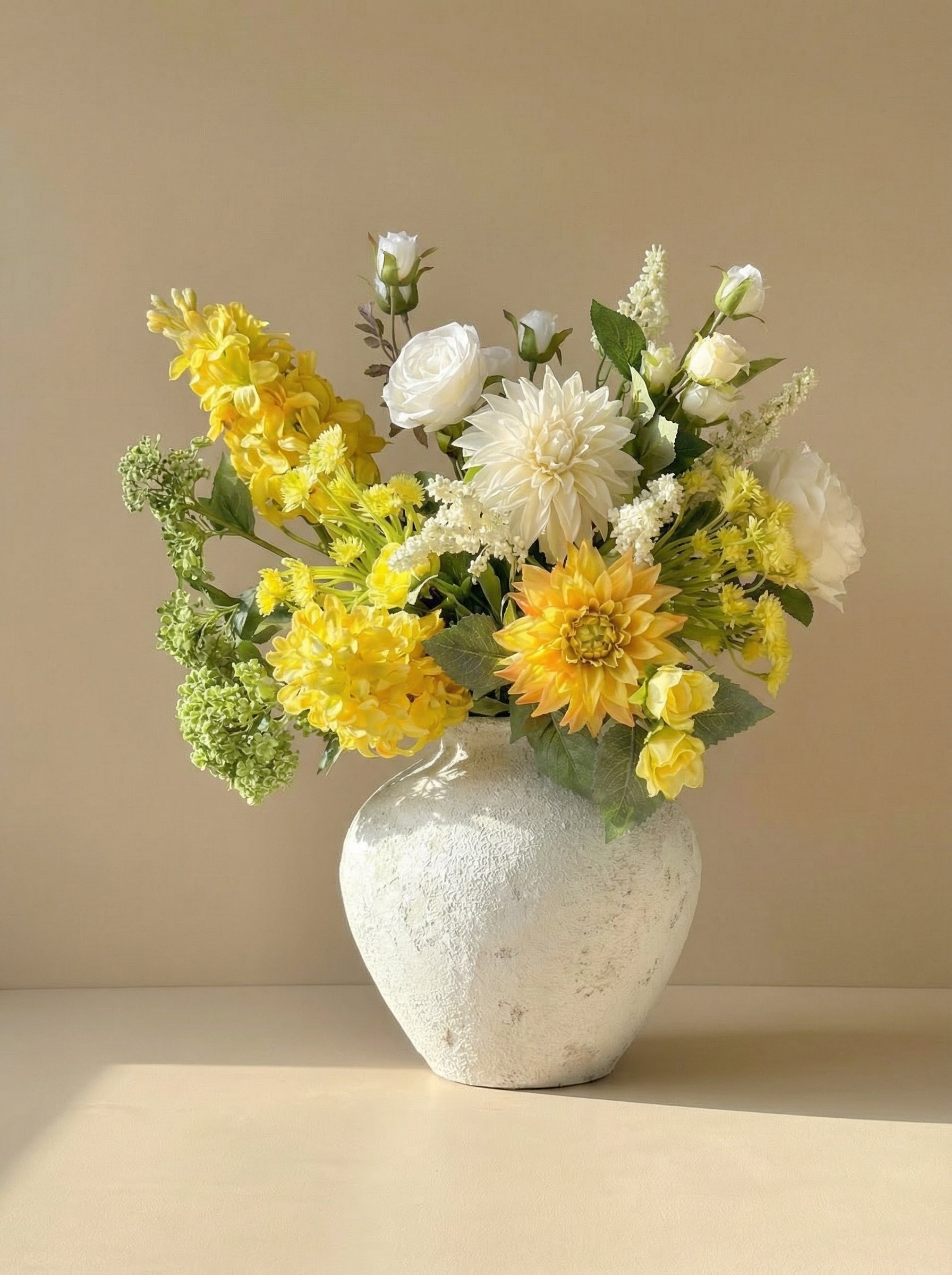 Bouquet of yellow and white flowers in a textured white vase on a beige surface with a beige background