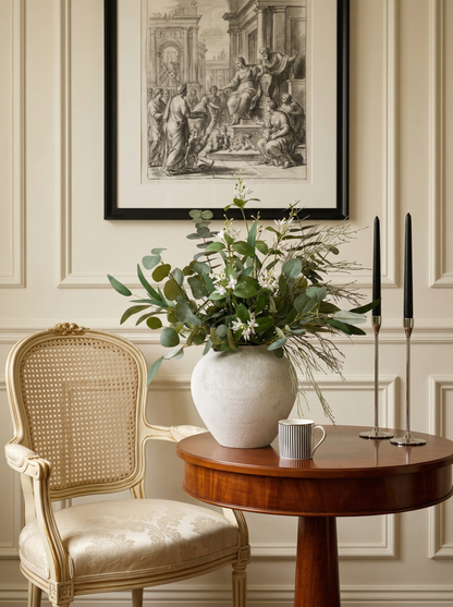 Decorative setting with a vase of flowers, chair, and table against a wall with framed artwork.
