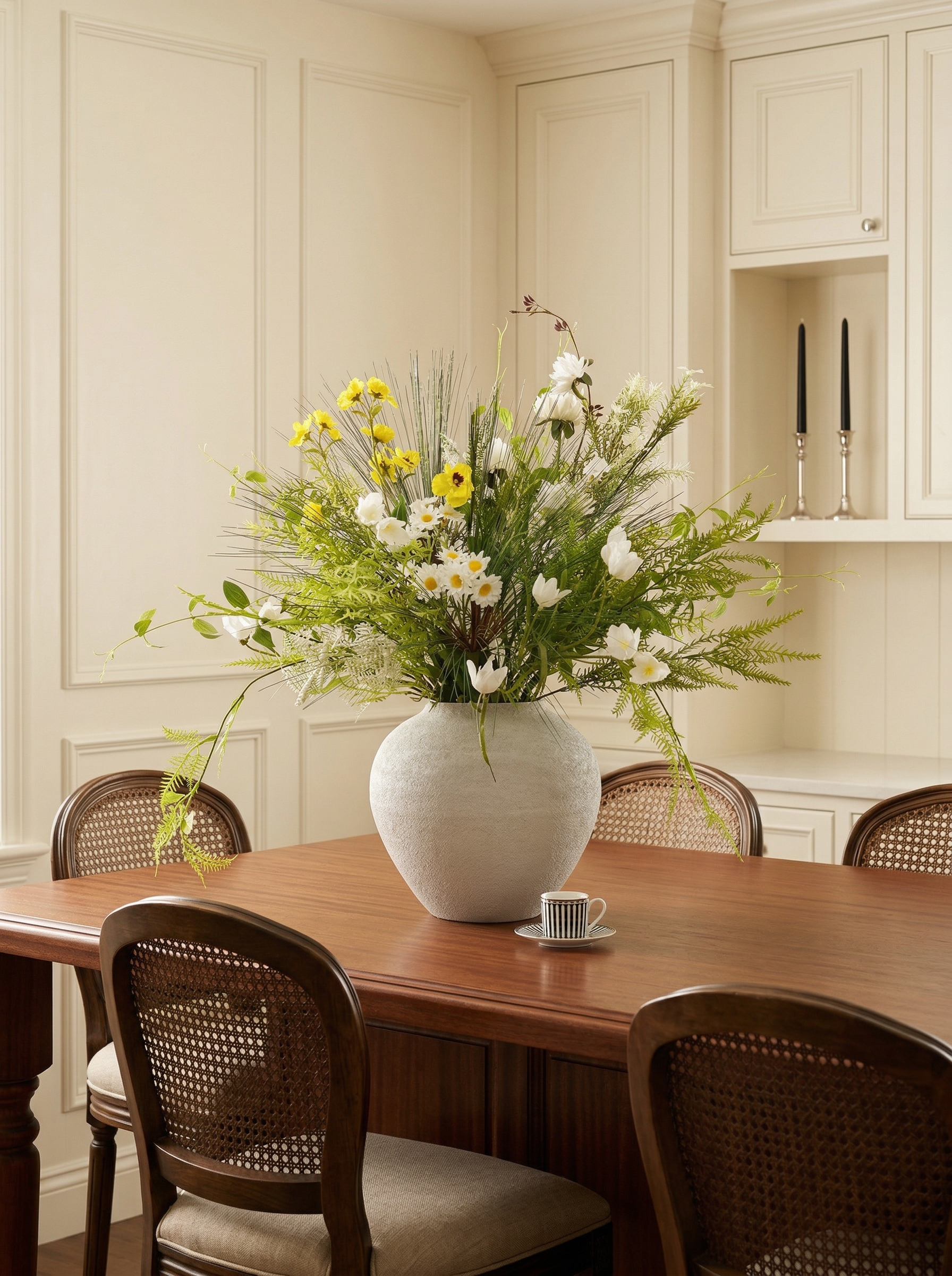 Dining room with a wooden table, white vase with flowers, and chairs.