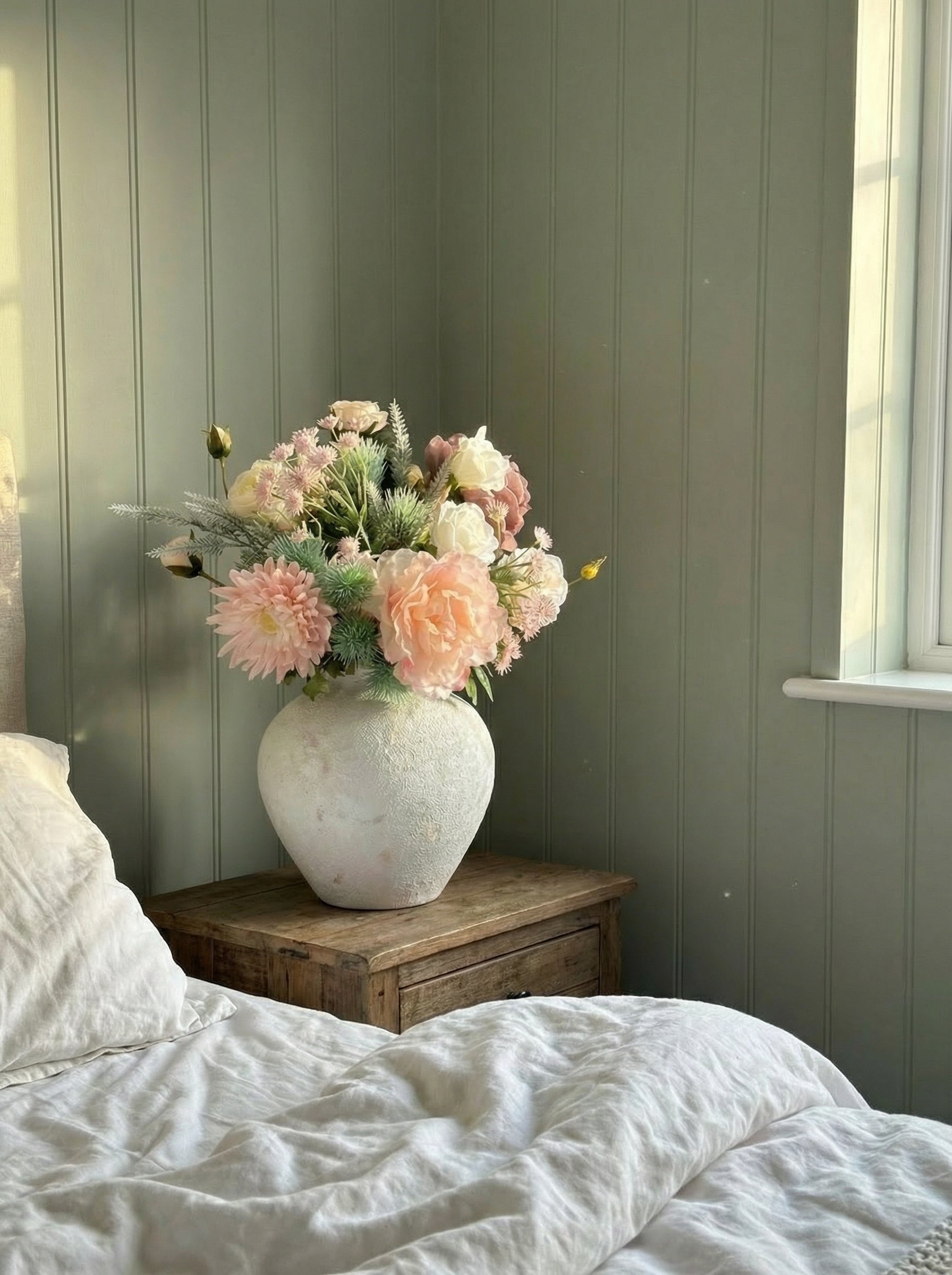 Floral arrangement in a vase on a wooden nightstand against a green paneled wall.