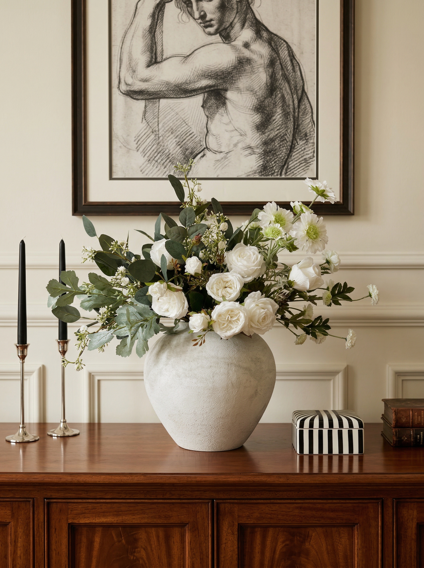 Floral arrangement in a vase on a wooden table with framed artwork in the background