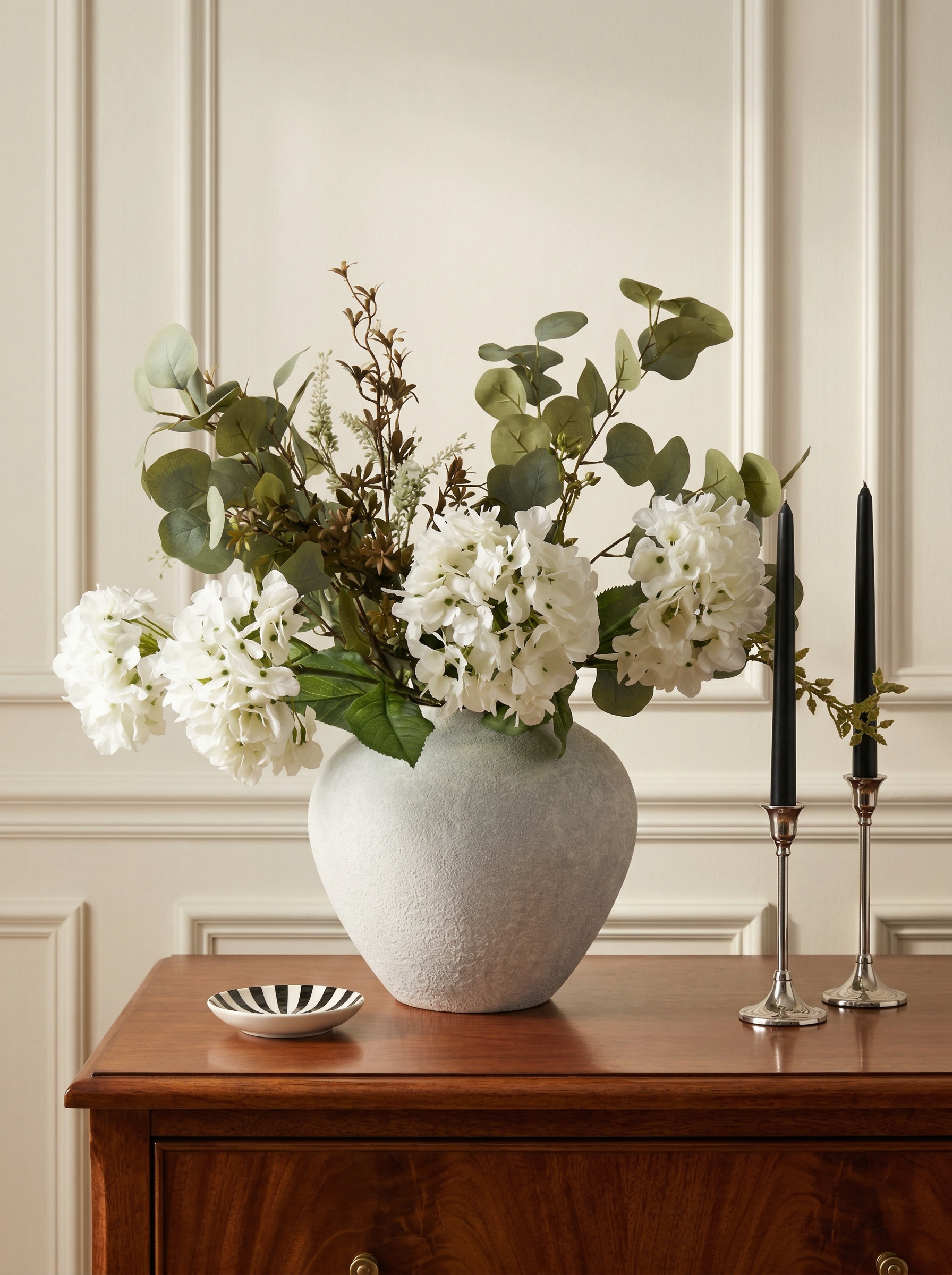 Vase with flowers on a wooden surface against a paneled wall