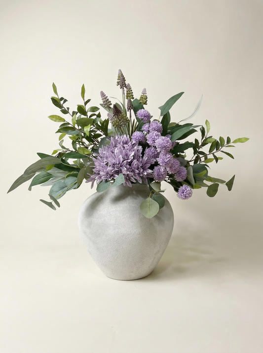 Vase with purple flowers and green leaves on a light background
