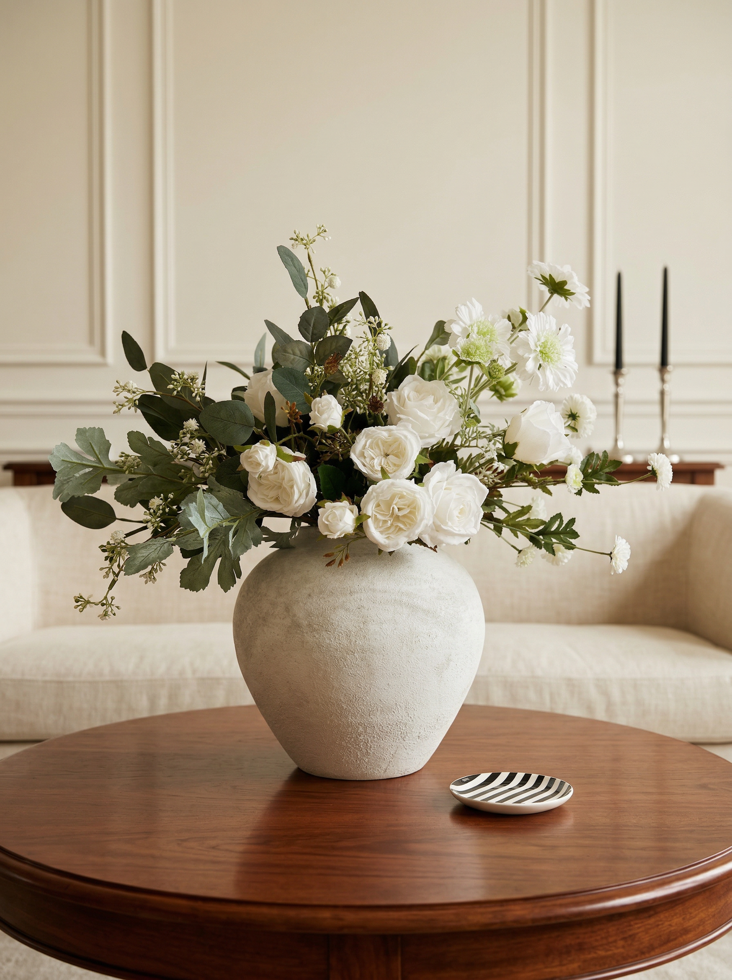 White vase with flowers on a wooden table in a room with a neutral color scheme.